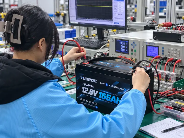 12.8V 165Ah LiFePO4 Battery Sample Validation for OEM Projects Illustration of a technician checking the terminals of a TUORDE 12.8V 165Ah LiFePO4 battery beside test instruments