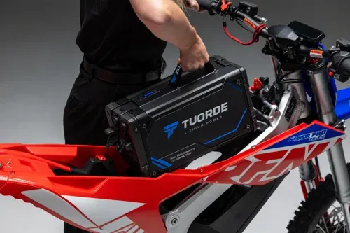 Motorcycle battery installation reference showing a TUORDE-branded pack being lowered into a red off-road motorcycle frame